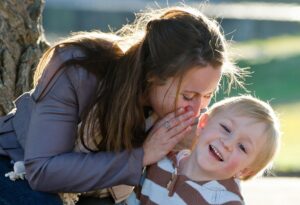 Mutter flüstert lachendem Kind etwas ins Ohr